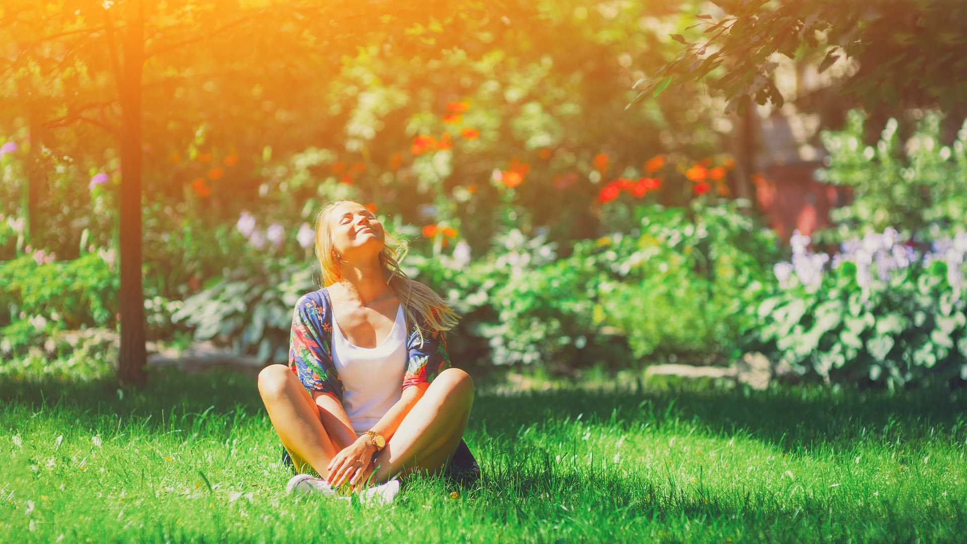 Happy woman sitting on the grass on sunny day among the flowers